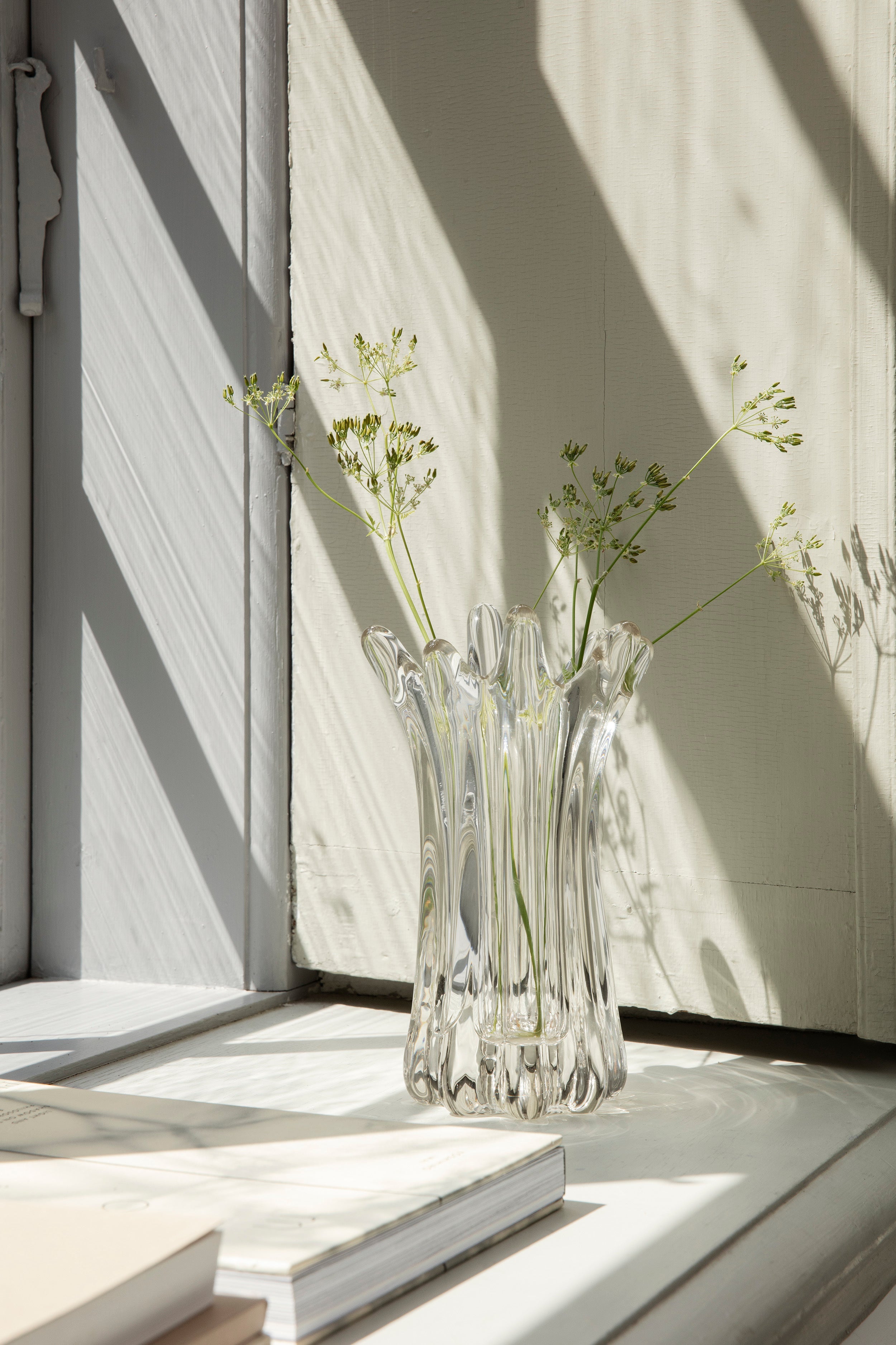 The Holo Vase by ferm LIVING with green flowers on a windowsill.
