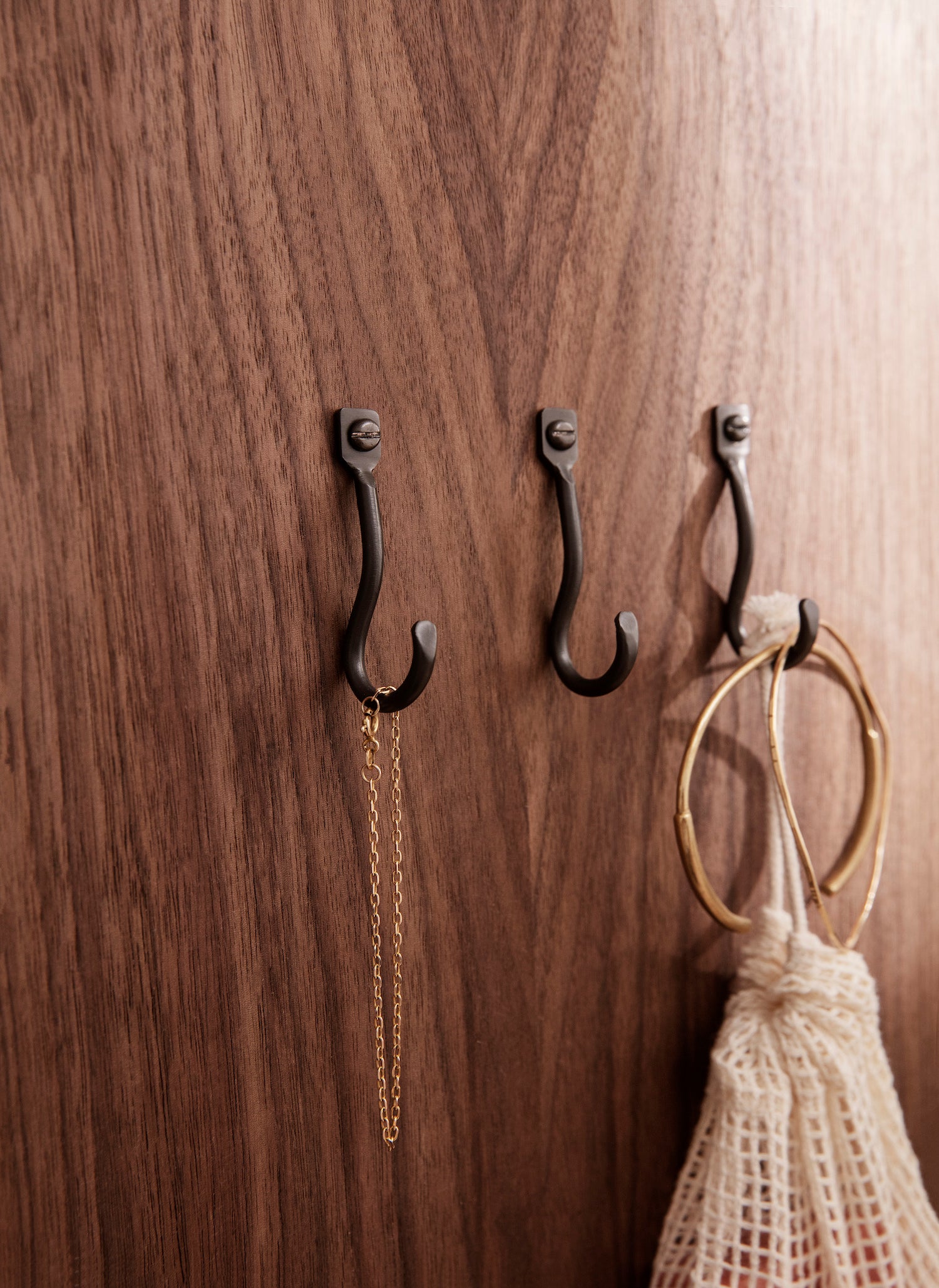 Organically shaped wall mounted hooks hand formed in black coated brass with a matte patina finish. 
