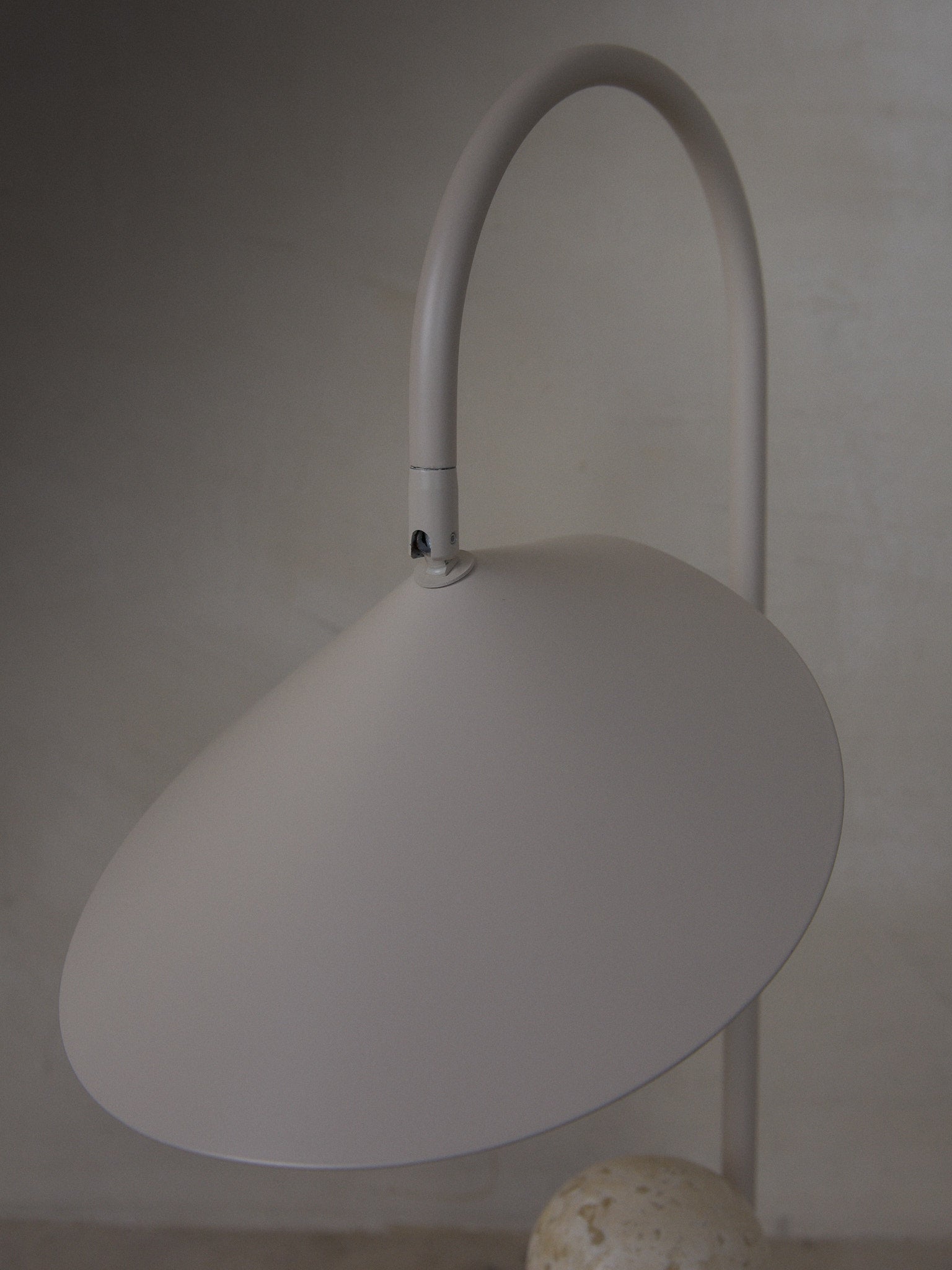 Arum Table Lamp. Statuesque, organically shaped table lamp with a beige travertine base and petal-like shade suspended from a curved metal arch. 