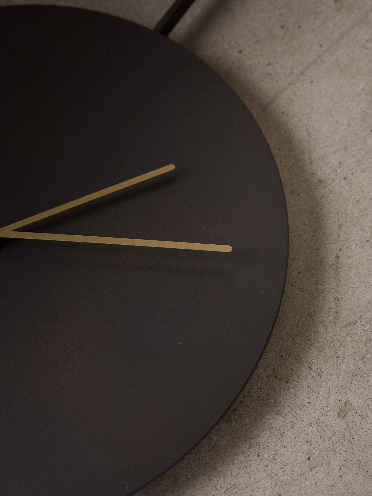 Trace Wall Clock. Minimalist, elegant wall clock with brass hands on a background of blackened steel, revealing only the constant, subtle movements of two hands reflecting the trace of time.