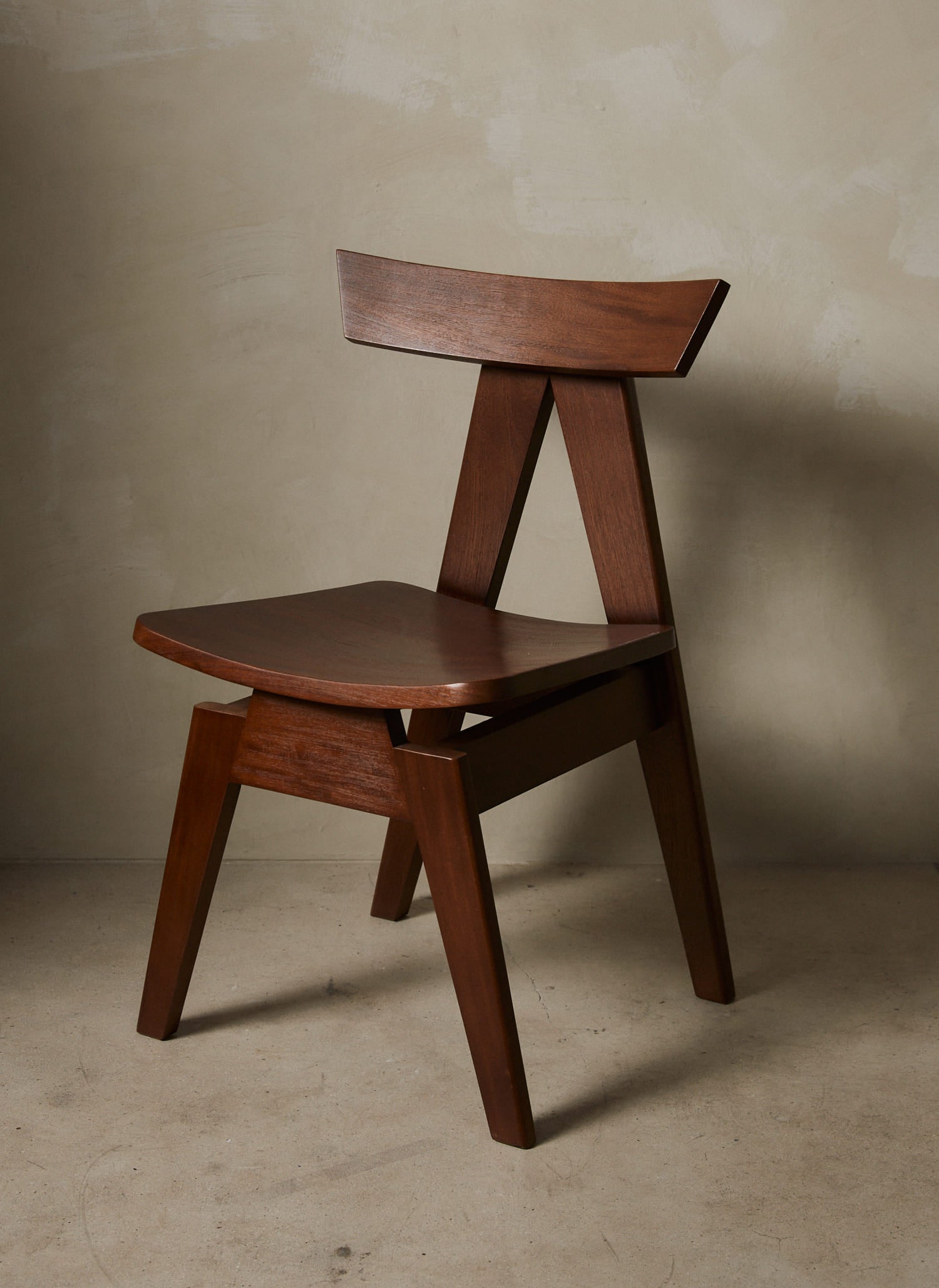  Clean, modernist dining chair with sharp angles sculpted from solid wood in a rich, deep brown finish.