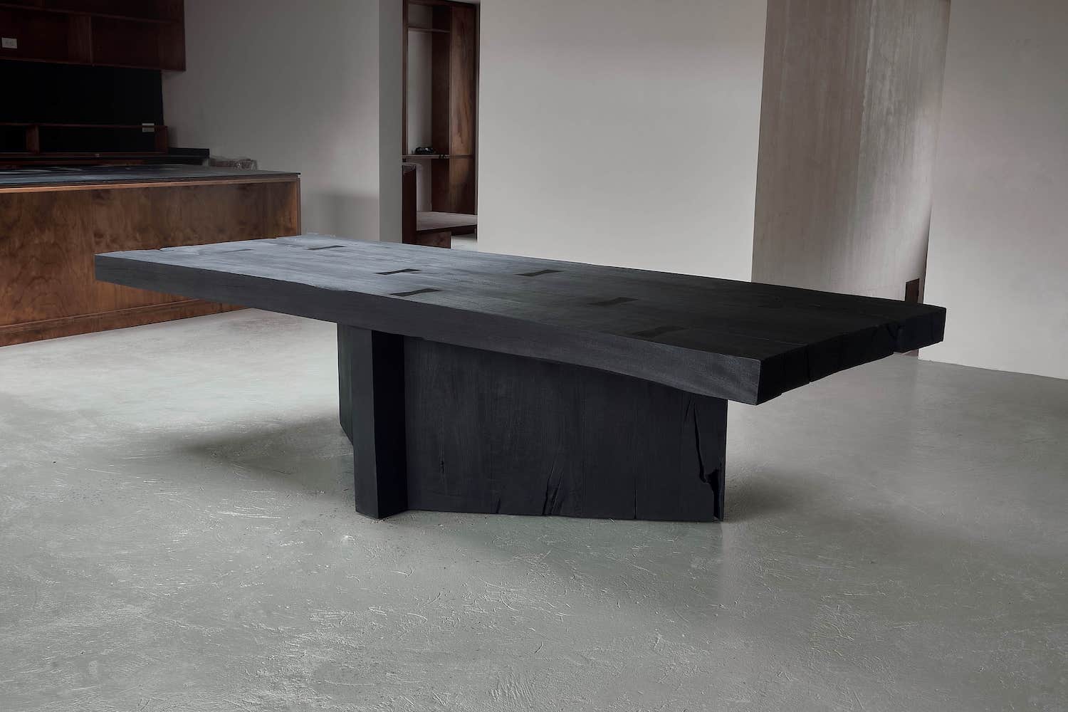  A monolithic wood dining table entirely burned by hand and made to withstand heavy user traffic, the Table Acros features a wide, rectangular surface and bold, asymmetric footing that feels wrought from nature.
