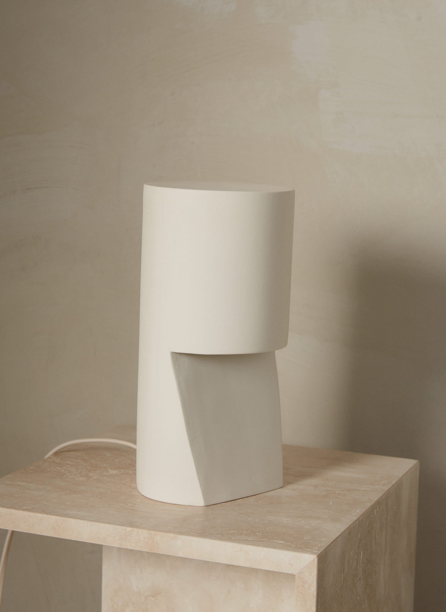 A cylindrical, hand sanded porcelain pillar table lamp in natural white.  Light shines subtly from a hollow outcropping in the porcelain body.  