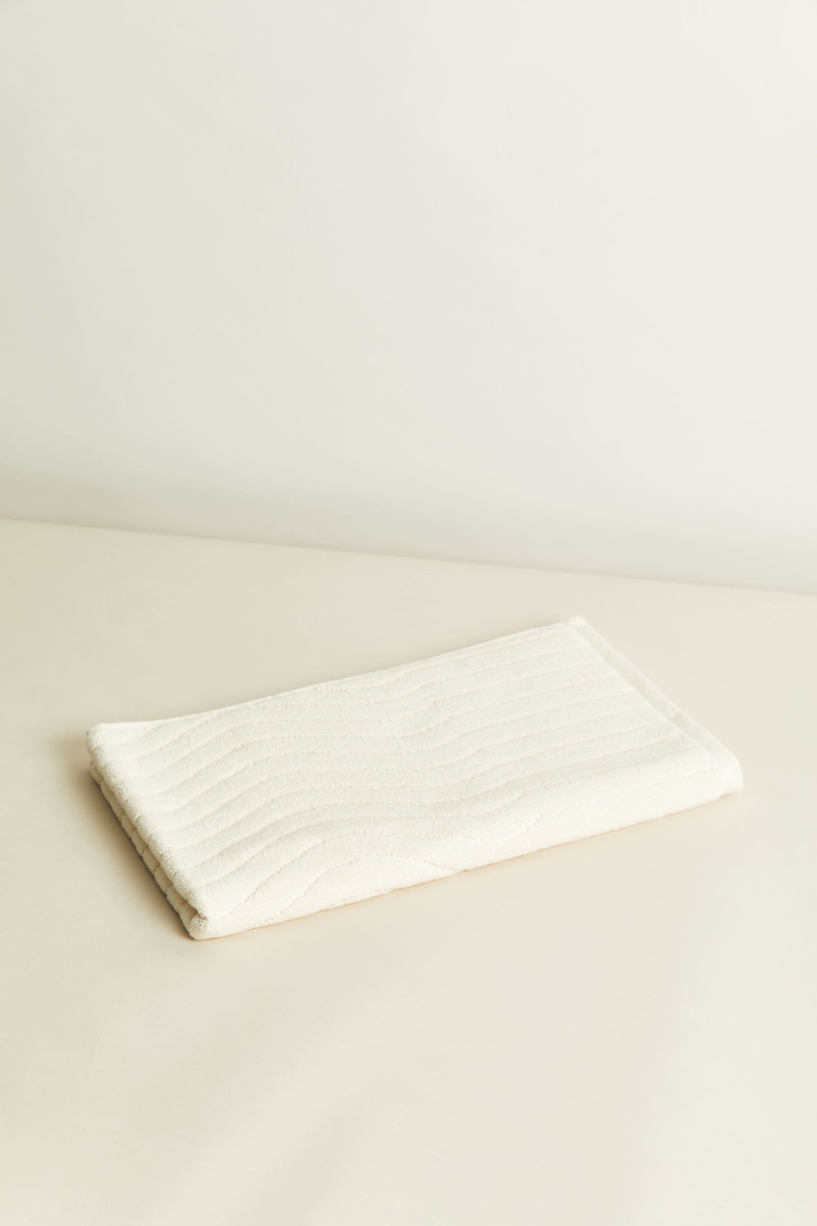 Erye Organic Cotton Bath Mat in ivory. An elevated, everyday bathroom essential with a unique textural pattern reminiscent of movement over skimmed water. Luxuriously soft, 100% organic cotton hand.