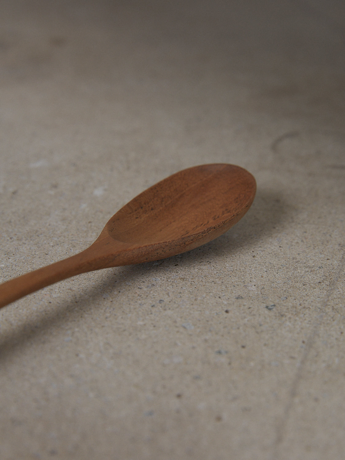 Elegant, elongated mixing spoon with arched handle, hand carved from natural teak wood.
