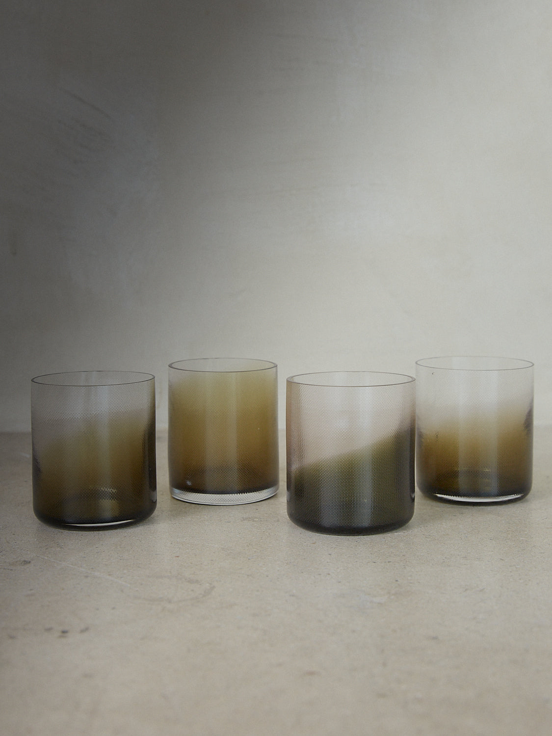 Smoke Green Raw Glass Set. Set of four tumbler glasses mouth blown into raw woven molds, textured and shaped by soft textile copper and accented with a smoke green gradient color. 