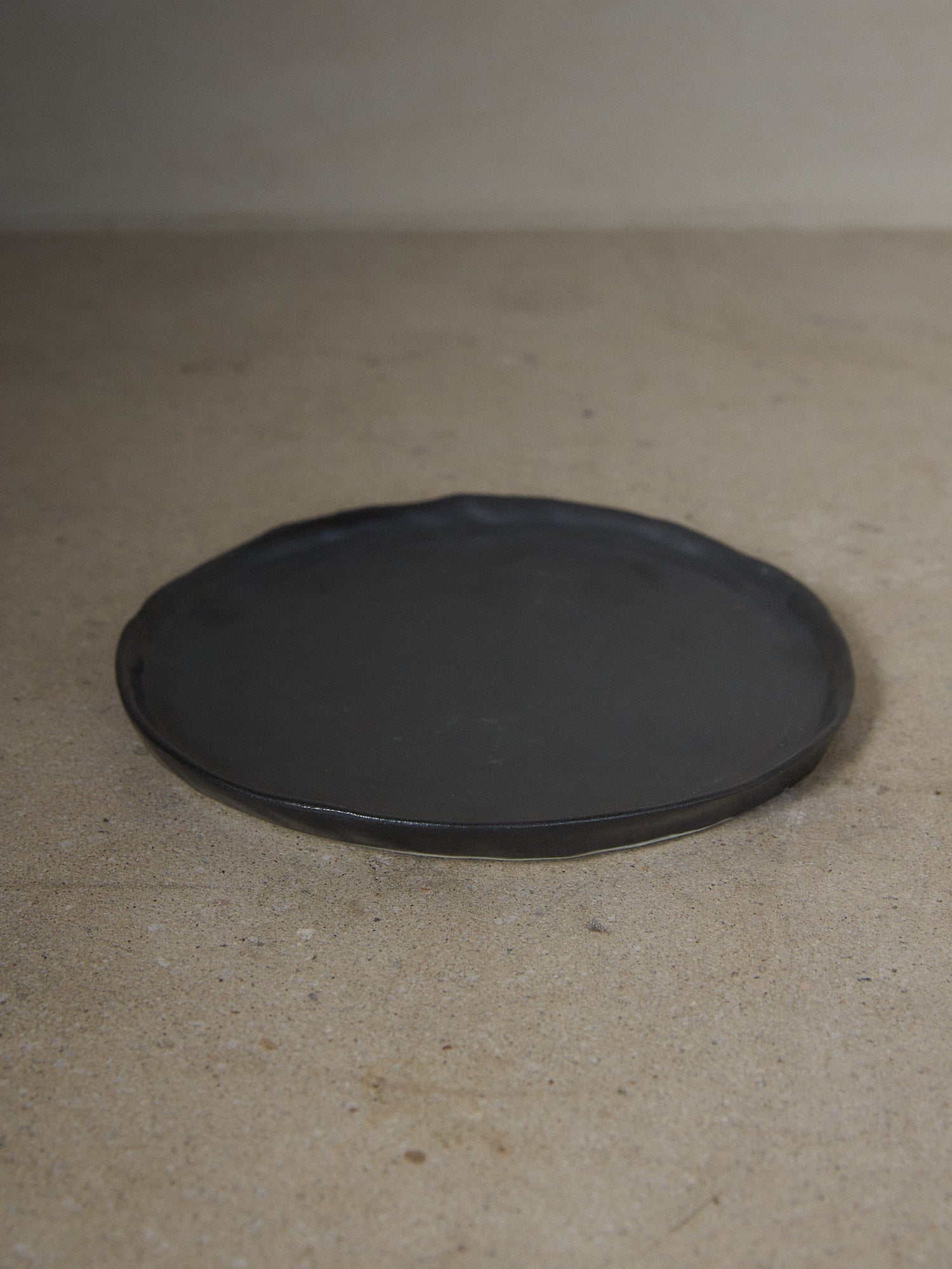 Raw Black Salad Plate. A hand-formed stoneware salad plate recalling the organic and natural world with perfectly imperfect edges in a classic matte black finish.