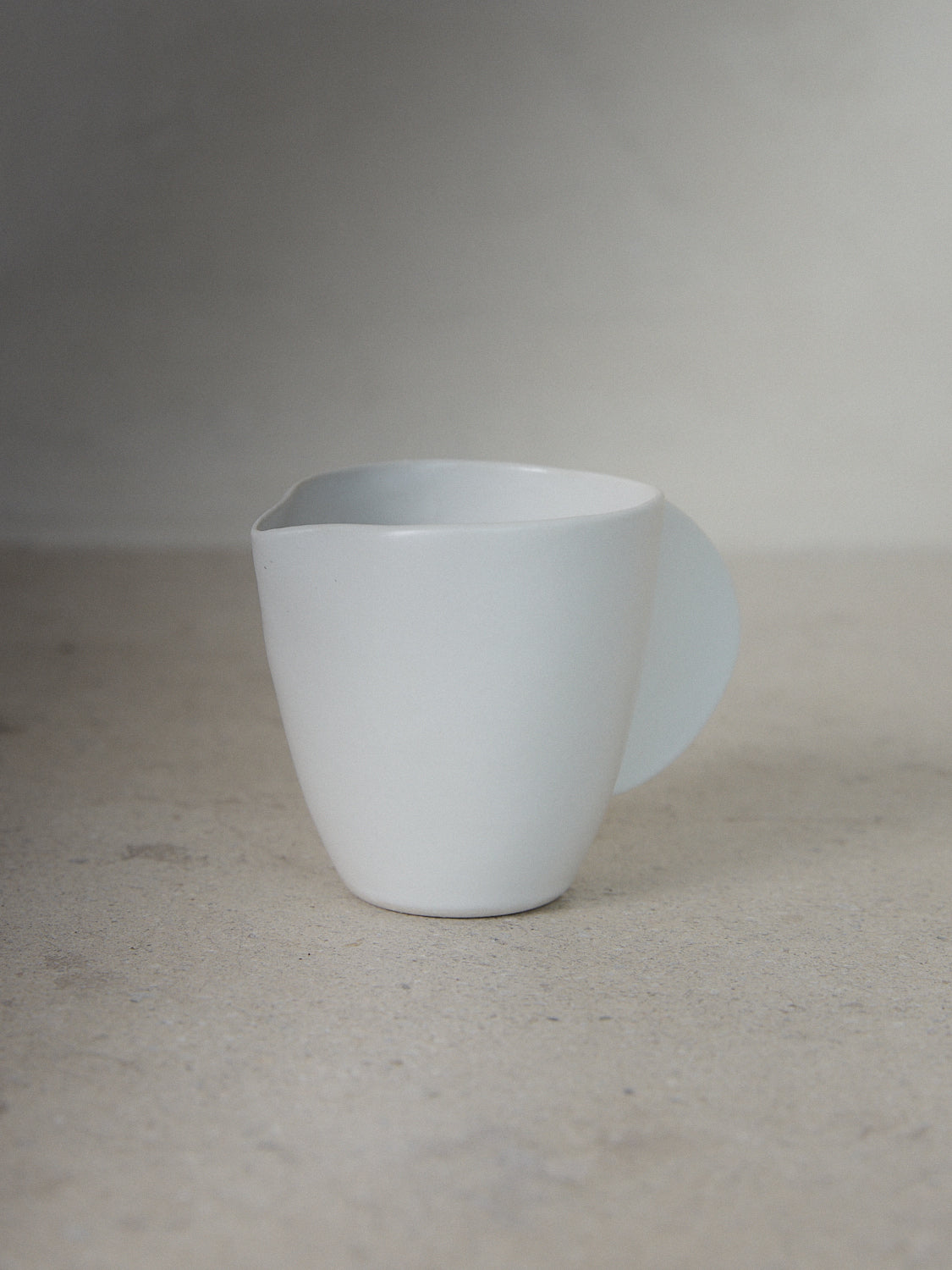 Raw Creamer. Exclusively ours. Hand sculpted coffee creamer jar with a pinched spout and solid, semicircle handle in matte, milky white stoneware.