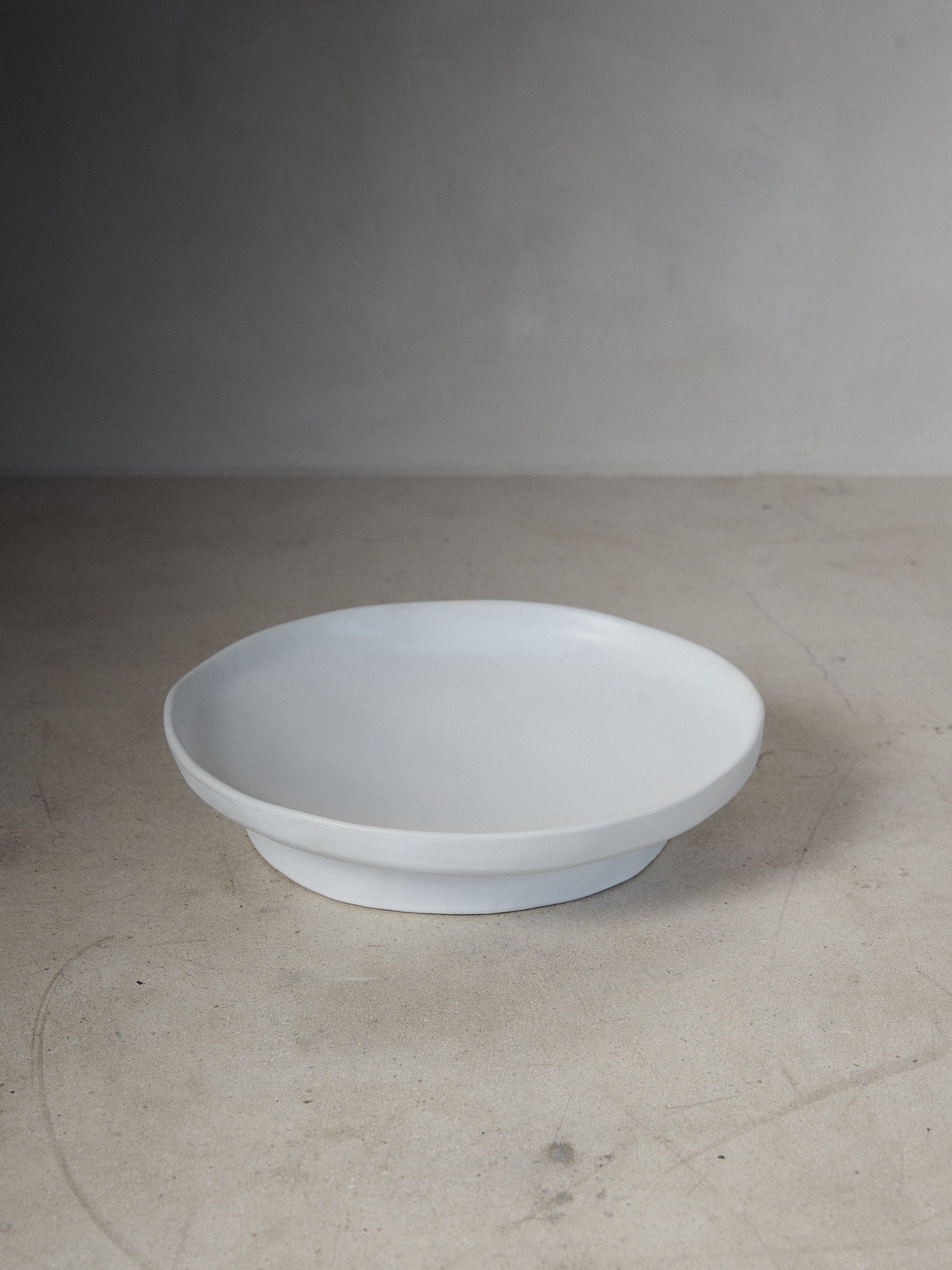 Raw Small Footed Platter. A hand-formed, wide rimmed platter recalling the natural world with perfectly imperfect edges atop a solid, footed base in versatile matte white stoneware.