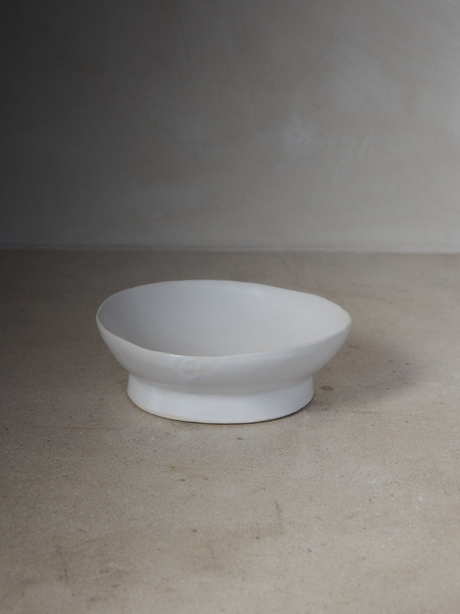 çRaw Small Footed Platter. A hand-formed rimmed platter recalling the natural world with perfectly imperfect edges atop a solid, footed base in versatile matte white stoneware.