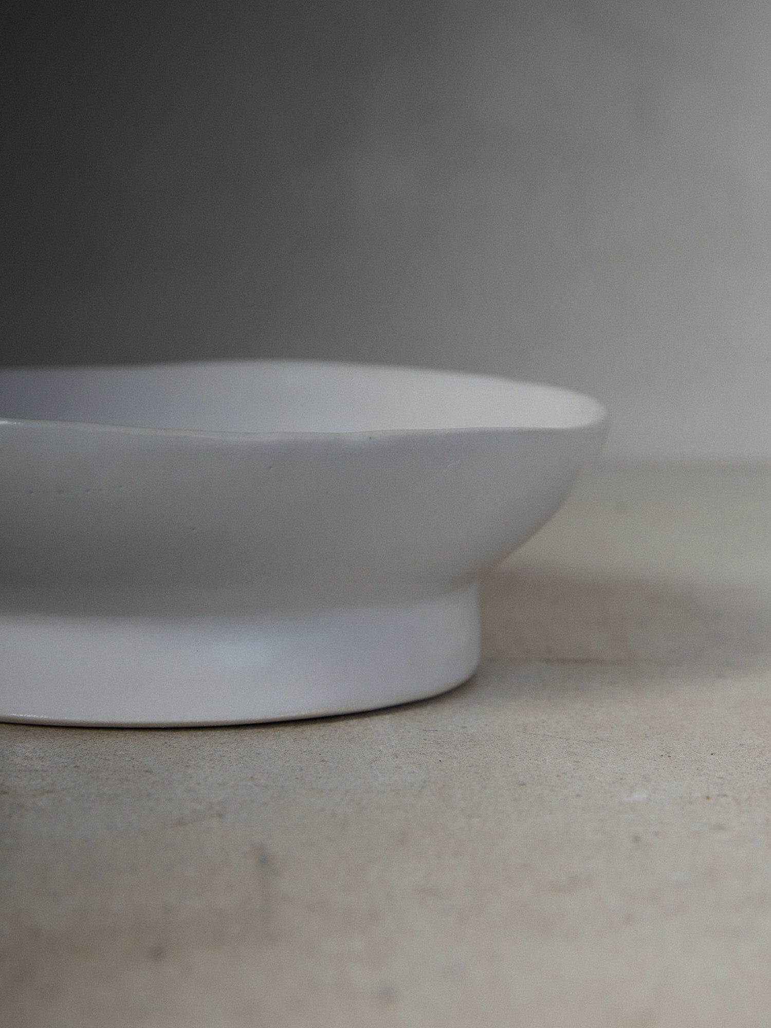 Raw Small Footed Platter. A hand-formed rimmed platter recalling the natural world with perfectly imperfect edges atop a solid, footed base in versatile matte white stoneware.